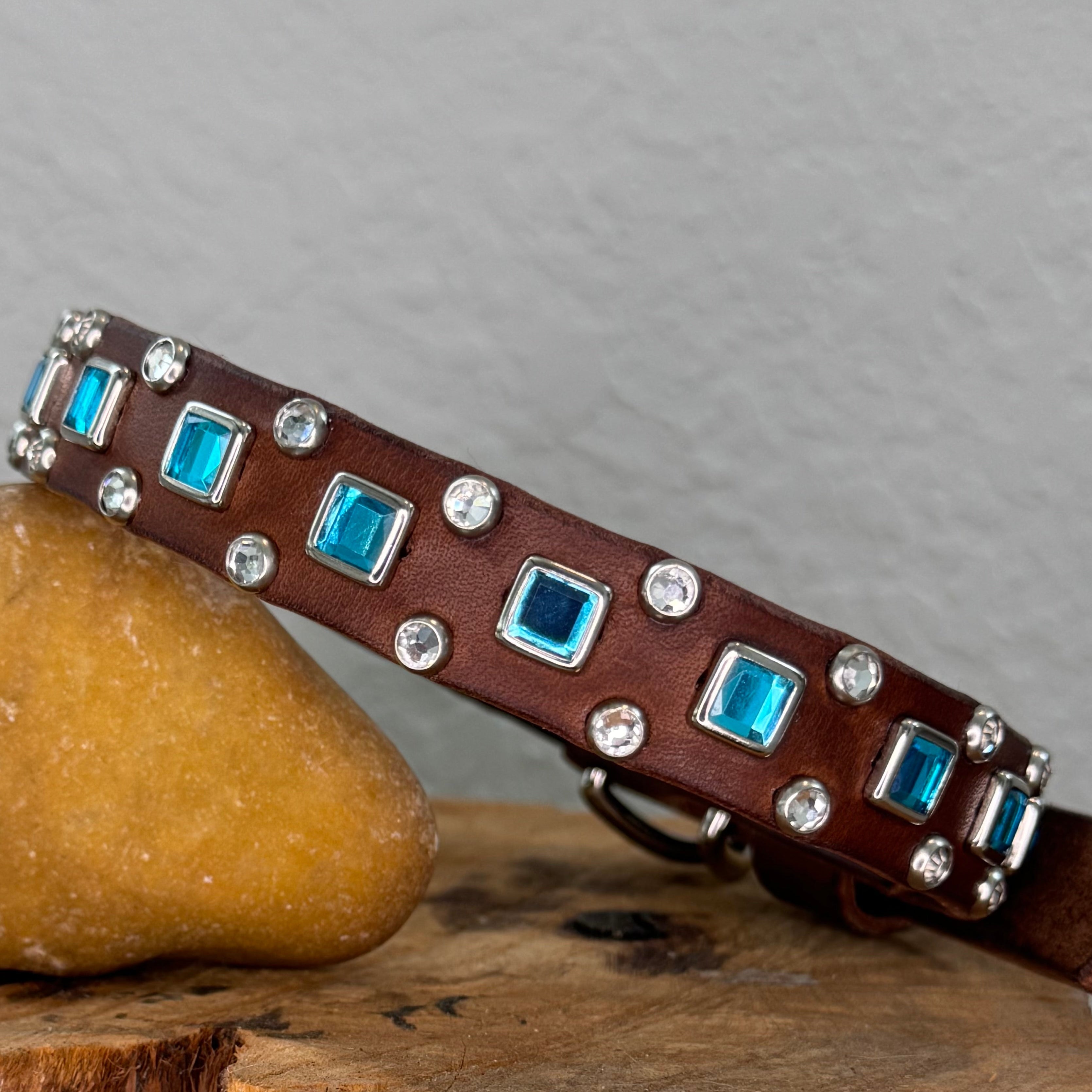 Brown leather dog collar with blue stones and silver studs on a wooden block.