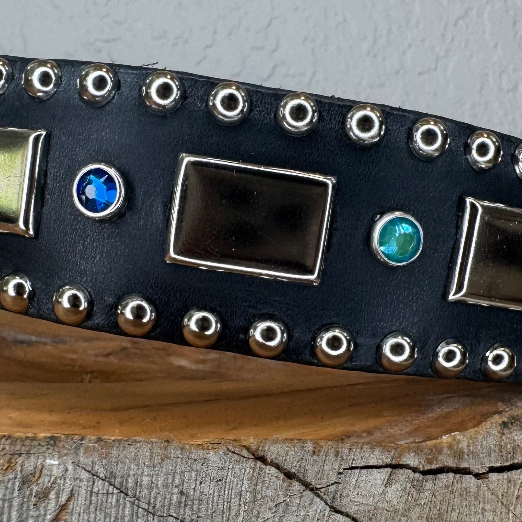 Black leather dog collar with metallic studs and gemstones on a wooden surface.