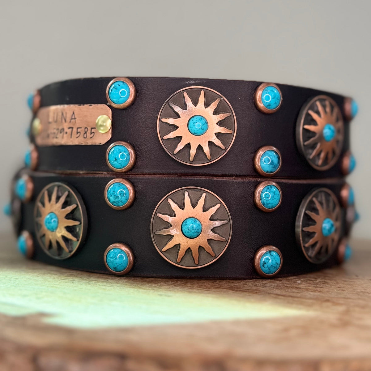 Brown leather dog collar with Native Sun conchos and turquoise cabochons on a wooden surface