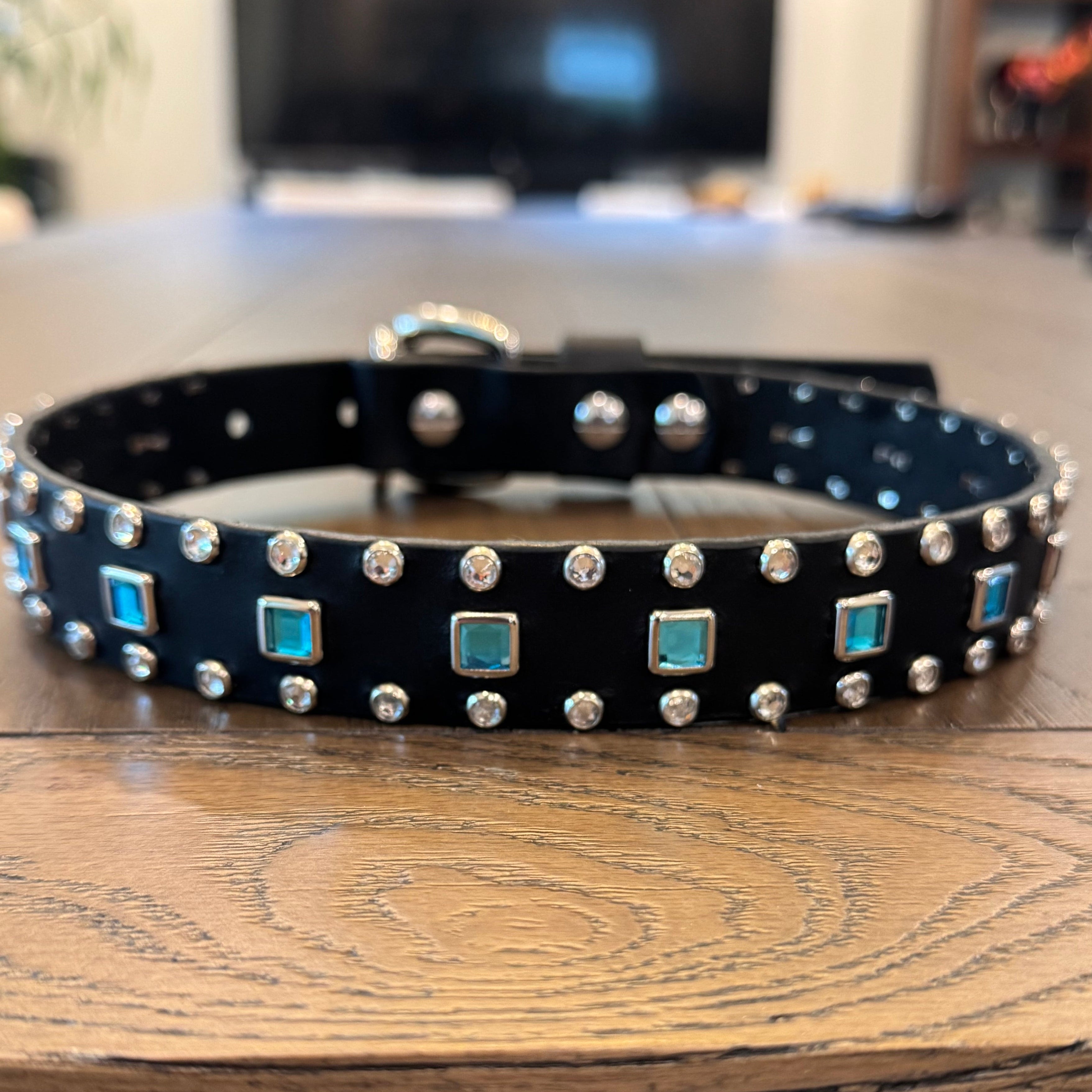 Black dog collar with silver studs and turquoise stones on a wooden surface.