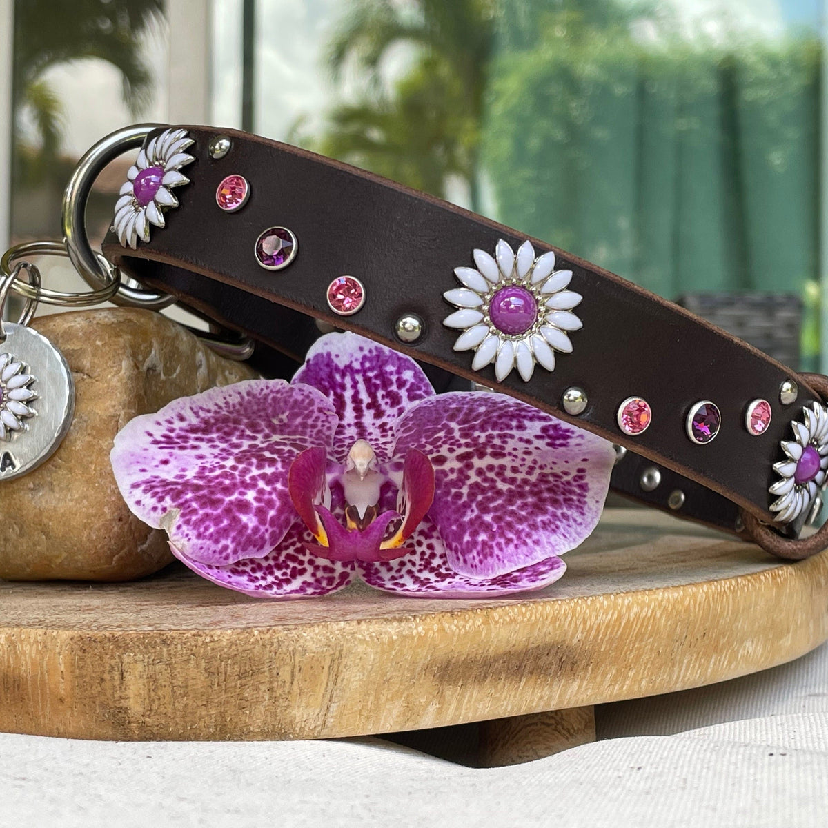 Decorative dog collar with flowers and a keychain on a wooden surface with a blurred outdoor background