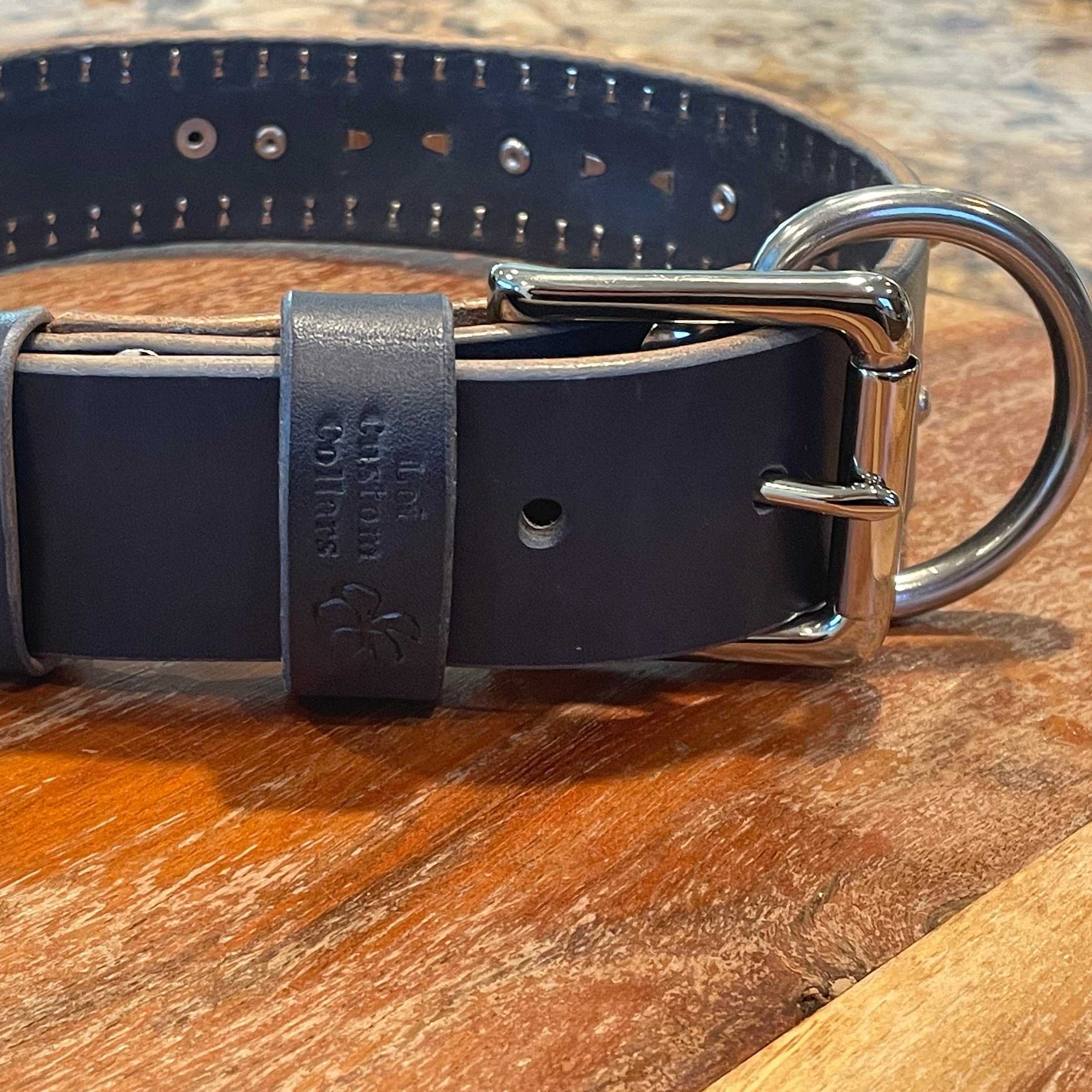 Navy blue leather dog collar with metal hardware on a wooden surface