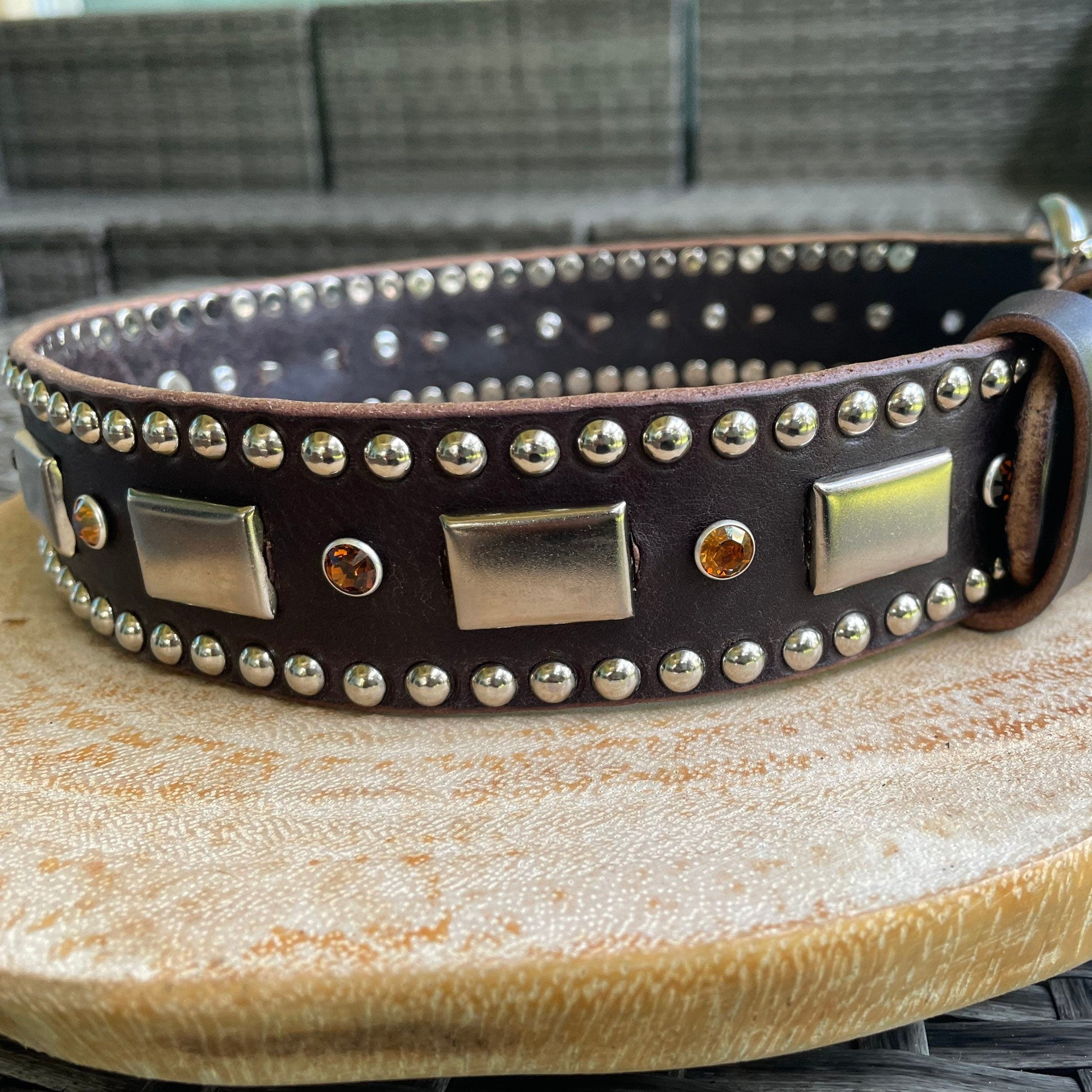 Brown leather dog collar with metal studs and buckles on a wooden surface.