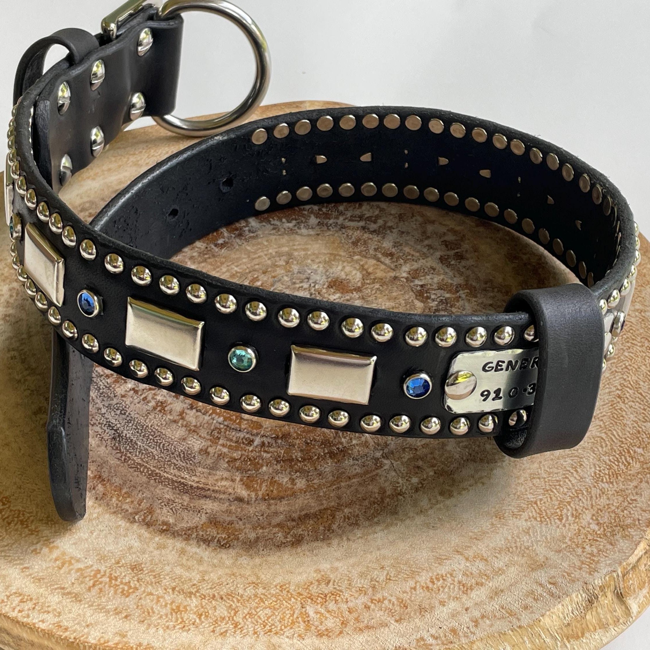 Black leather dog collar with decorative studs and metal plates on a wooden stand.