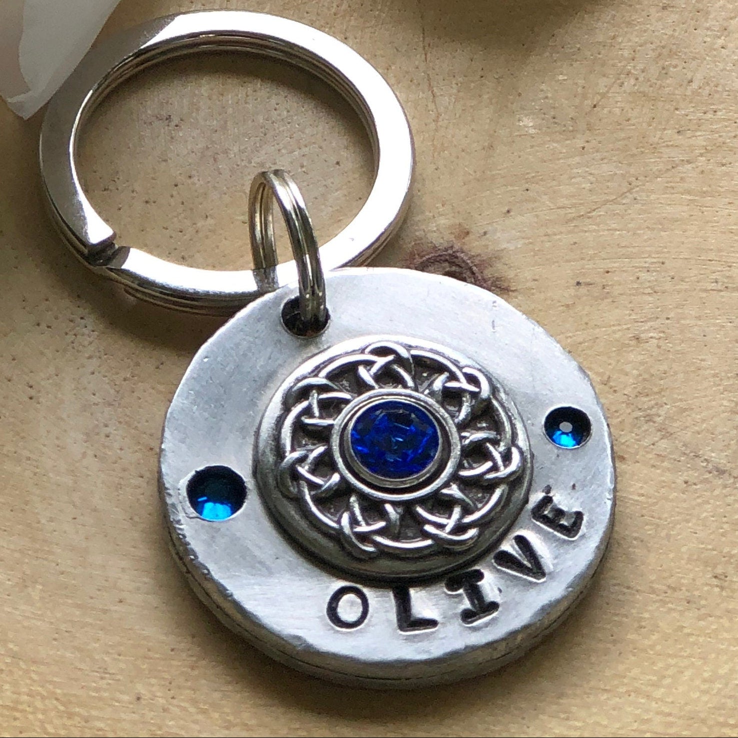 Silver keychain with a blue stone and 'LOVE' engraving next to a white flower on a wooden surface.