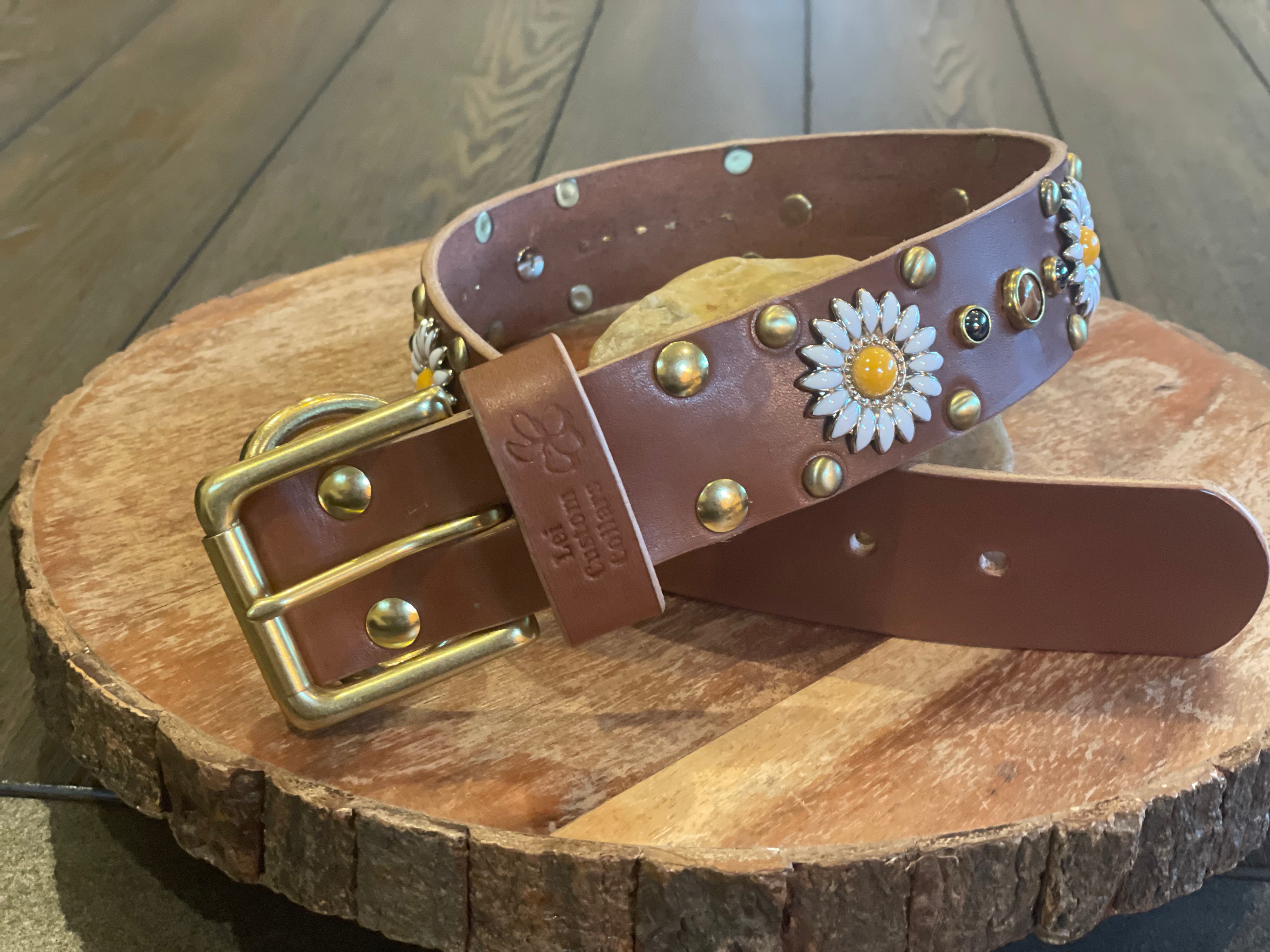 Handcrafted brown leather dog collar with brass buckle, daisy concho accents, and metal studs, luxury custom pet collar photographed on rustic wood surface.