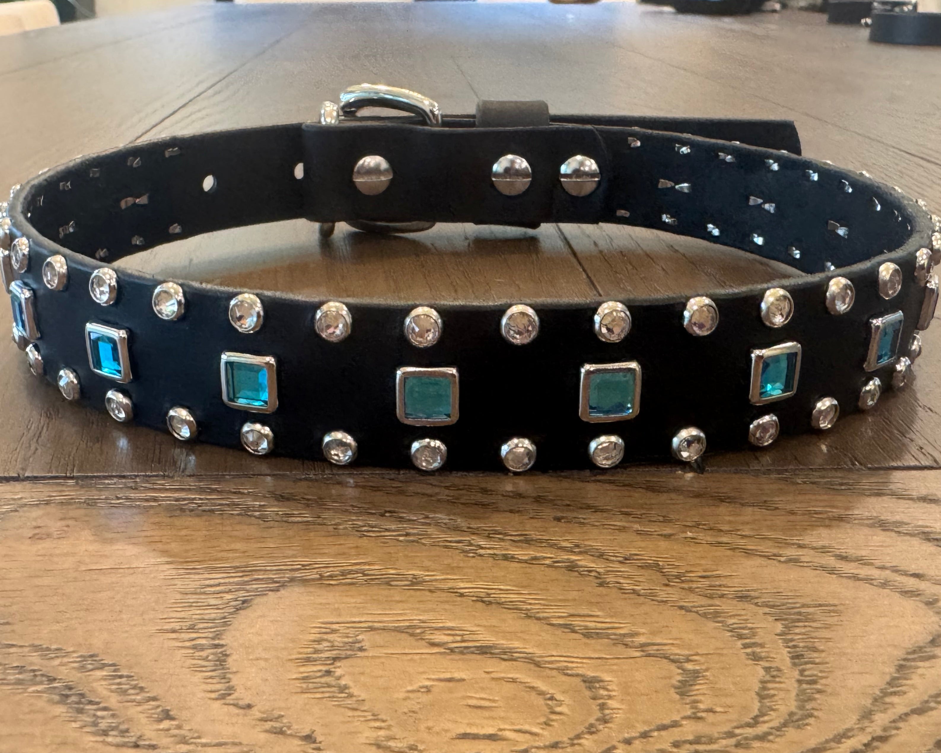Black leather dog collar with silver studs and blue accents on a wooden table.