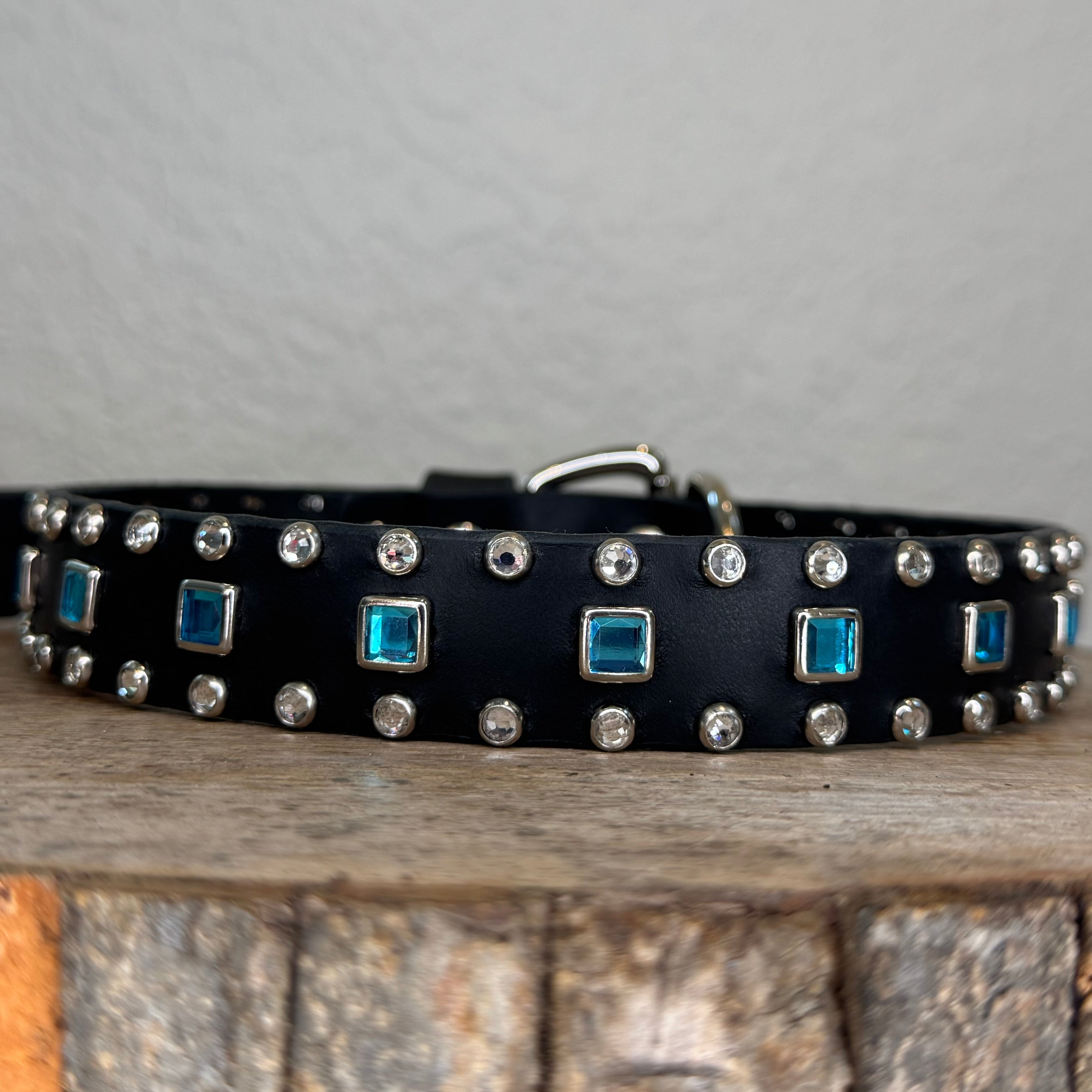Black studded belt with blue stones on a wooden and stone background