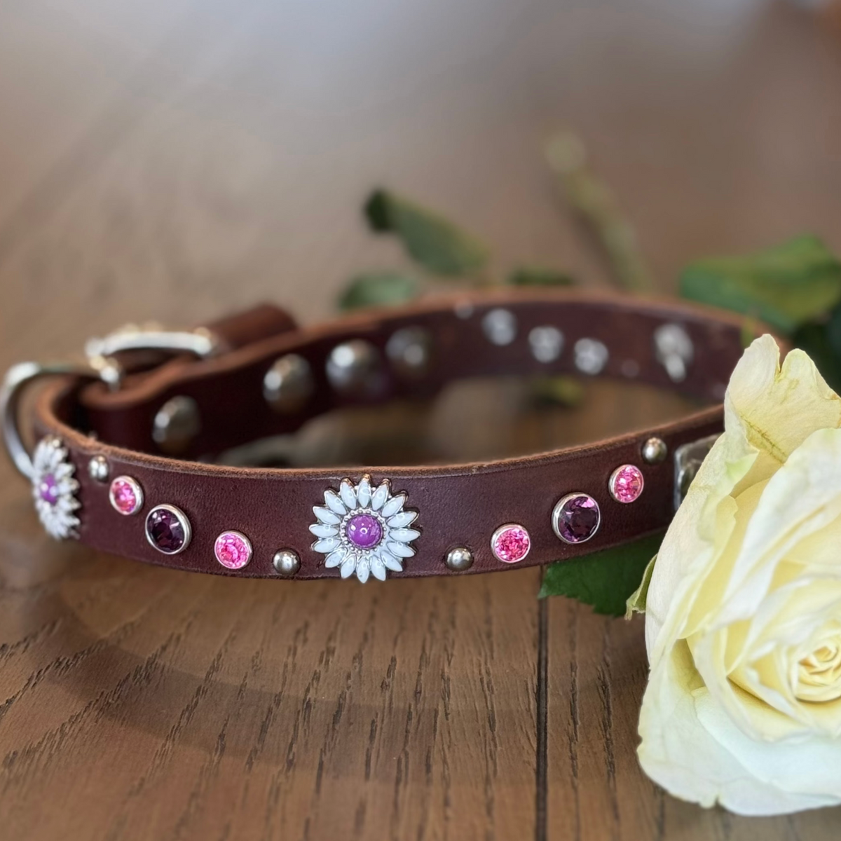 A custom brown leather dog collar decorated with pink and white rhinestones, displayed on a wooden surface next to a white rose. The image is a screenshot of a product customization page showing various metadata and editing options on the right.