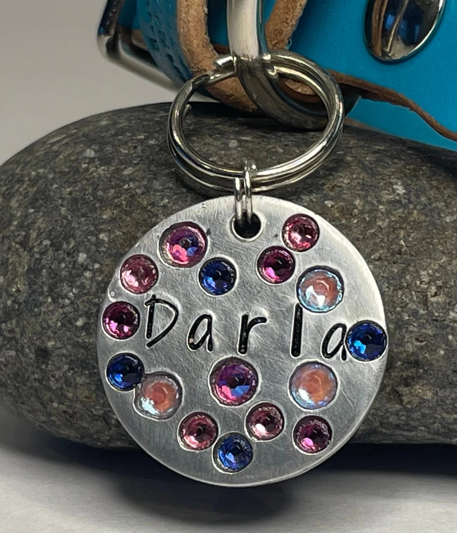 Handcrafted round silver dog ID tag engraved with the name “Darla,” accented with pink, blue, and iridescent crystals, displayed on a luxury leather dog collar for an elegant custom pet accessory look.